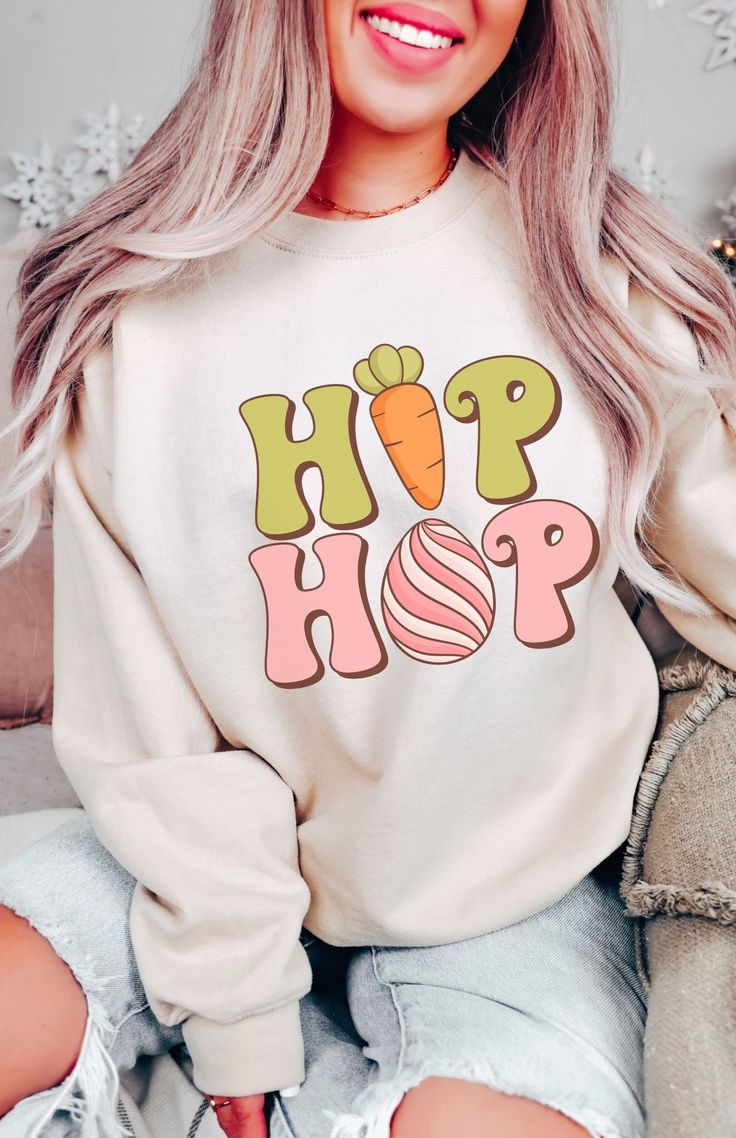 Super cute and comfy, this Easter Bunny Hip Hop Sweatshirt features a retro Easter Bunny graphic. With a cute Easter Bunny Easter Eggs graphic on the front and a cozy soft fleece interior, this Bunny Sweatshirt is sure to be a new fave. Available in Irish Green, Sand, Light Blue and Dark Heather colors. Fit is true to size, for oversized fit size up. Free Shipping USA. Be Cozy! Easter Bunny Hip Hop Sweatshirt 50% cotton, 50% polyester Medium-heavy fabric  Loose fit crewneck sweatshirt Machine wa Easter Sweatshirt Ideas, Retro Long Sleeve Tops With Letter Print, Retro White Sweatshirt For Spring, White Retro Sweater With Letter Print, Retro White Sweater With Letter Print, Fun Cotton Sweater With Graphic Print, Cute Fall Streetwear Tops, Playful Tops With Letter Print For Fall, Playful Letter Print Tops For Fall