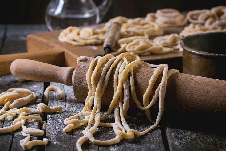 pasta being rolled up on a wooden table next to a rolling pin and measuring spoon