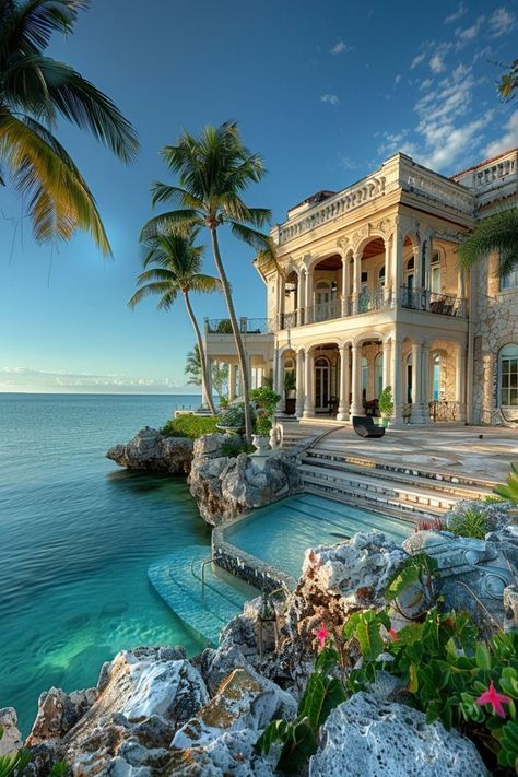 an oceanfront home with palm trees and blue water in the foreground, surrounded by rocks