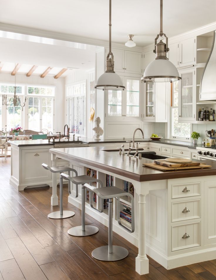 a large kitchen with white cabinets and wood flooring is pictured in this image, there are stools around the island