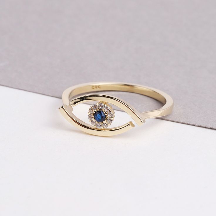 The 14K Evil Eye Ring is a stunning and intricate piece of jewelry that is perfect for any occasion. The ring features a beautiful Evil Eye design, with sparkling CZ diamonds and a vibrant blue sapphire. The Evil Eye is depicted on the ring, adding to its symbolism of protection and good luck. This ring is perfect for everyday wear or as a special occasion piece, and would make a thoughtful gift for any woman in your life. Whether you're looking for a gift for Christmas, Father's Day, Mother's D Gold Sapphire Stackable Rings For Promise, 14k Gold Ring With Diamond Eyes, Gold Sapphire Stackable Promise Rings, Diamond Jewelry With Diamond Eyes For Promise Ring, Elegant Silver Rings With Diamond Eyes, Elegant Rings With Diamond Eyes For Anniversary, Elegant Ring With Diamond Eyes For Anniversary, Elegant Formal Rings With Diamond Eyes, Anniversary White Gold Rings With Diamond Eyes