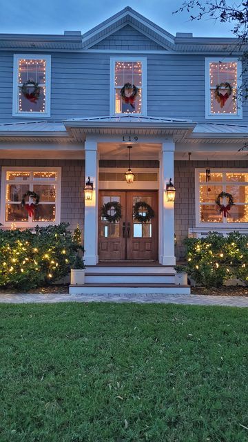 a house decorated for christmas with wreaths on the front porch and lights in the windows