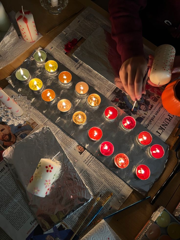 a person lighting candles on top of a table with papers and other items around it