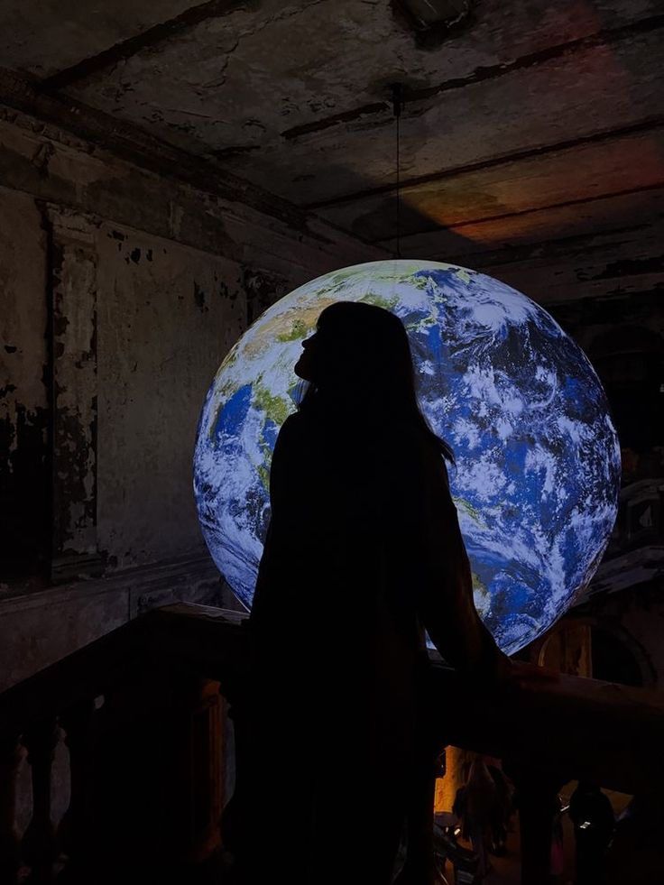 a person standing on a balcony looking at the earth projected into the wall behind them