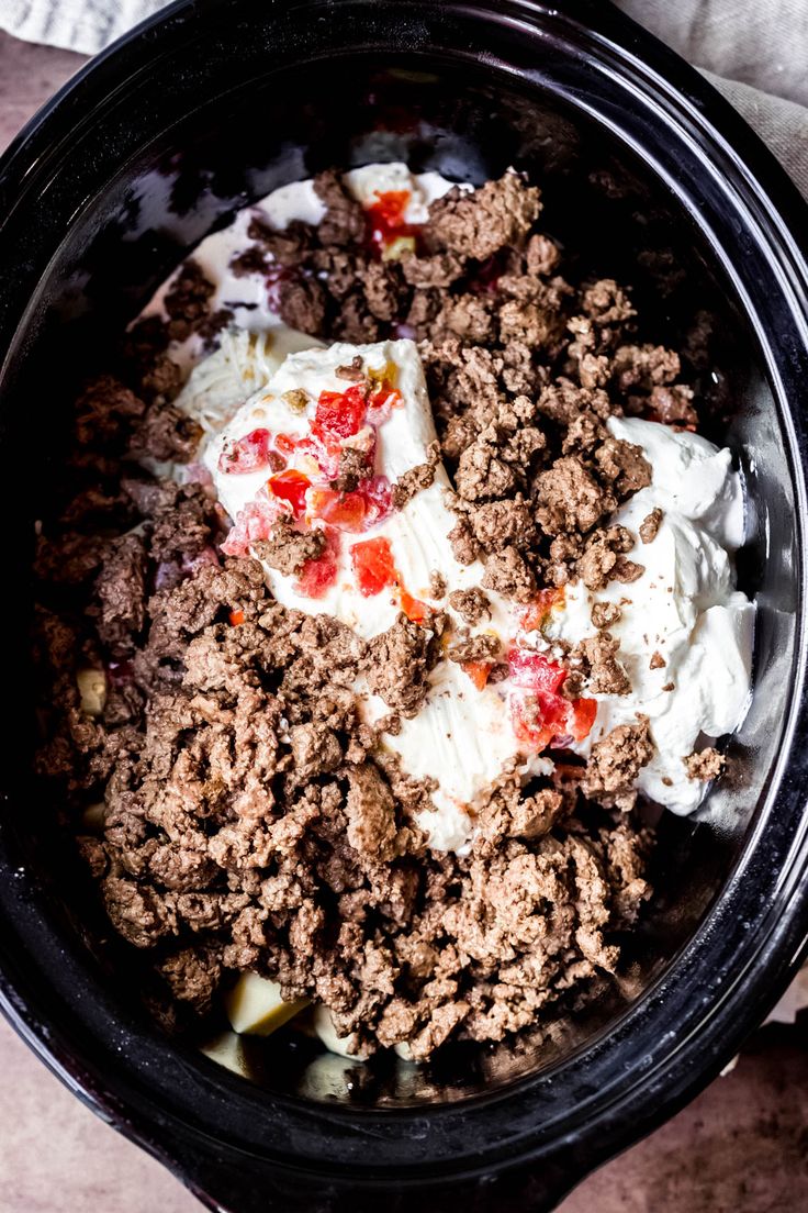 a black bowl filled with meat and cream on top of a wooden table next to a napkin