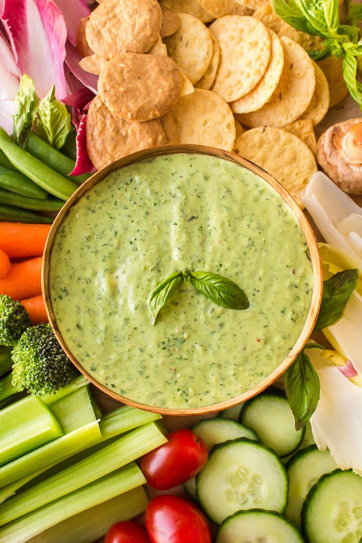 a bowl of dip surrounded by vegetables and crackers