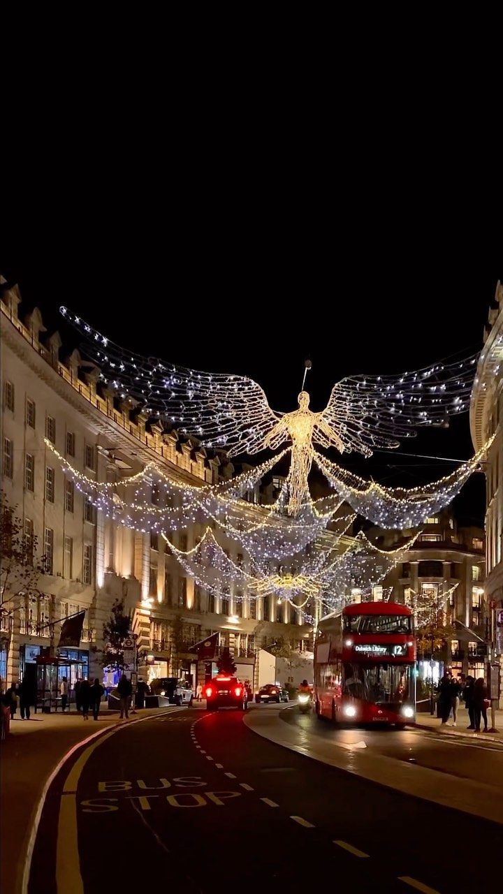 a city street is decorated with christmas lights and angel decorations, as people walk on the sidewalk