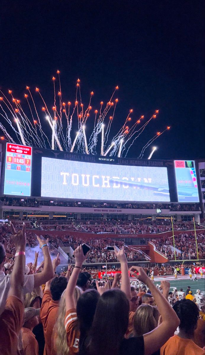 fireworks are lit up in the air above a crowd at a football game as spectators watch