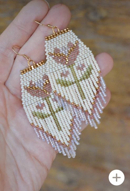 a hand holding a pair of beaded earrings in it's left hand, with flowers on them