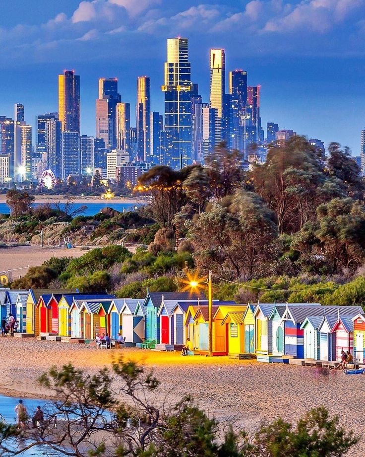 colorful beach huts line the shoreline in front of a city skyline