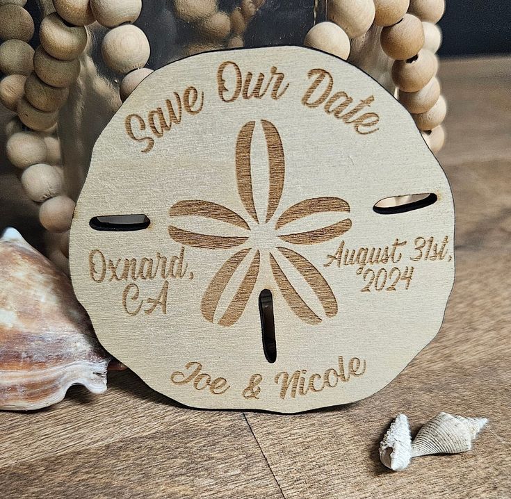 a wooden save our date sign on a table next to shells and seashells