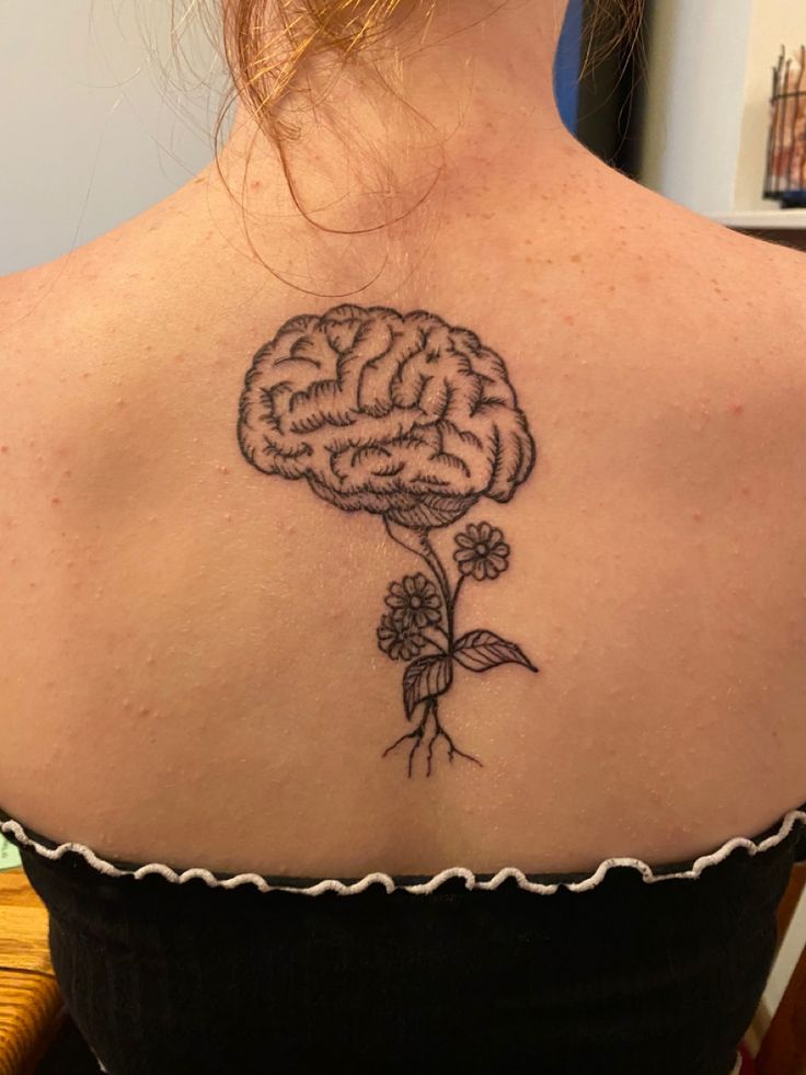 the back of a woman's shoulder with a flower and brain tattoo on it