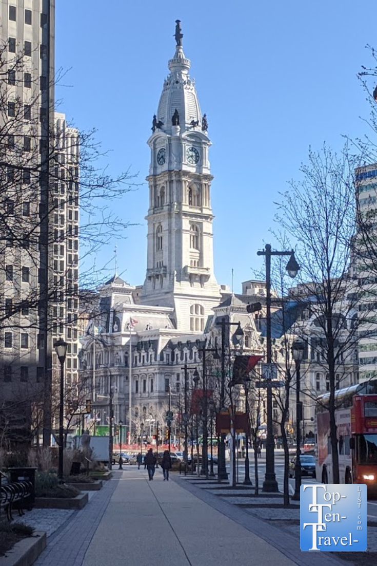 people walking down the sidewalk in front of a large building with a clock tower on top