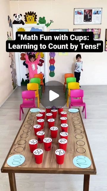 a wooden table topped with red cups filled with cupcakes next to colorful chairs