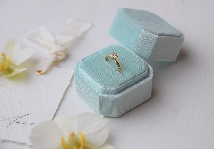 an open ring box sitting on top of a white table next to flowers and napkins