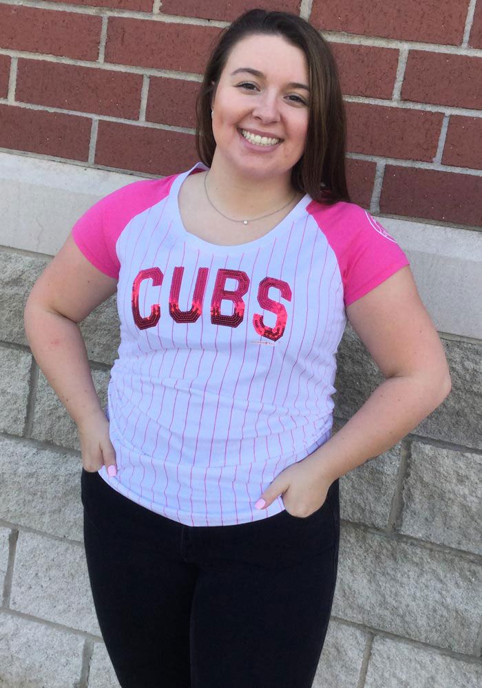 a woman standing in front of a brick wall wearing a pink and white shirt with the word cubs on it