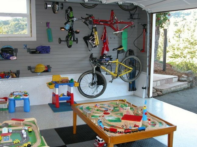 a garage with toys and bicycles on the wall, including a toy train table and two children's play tables