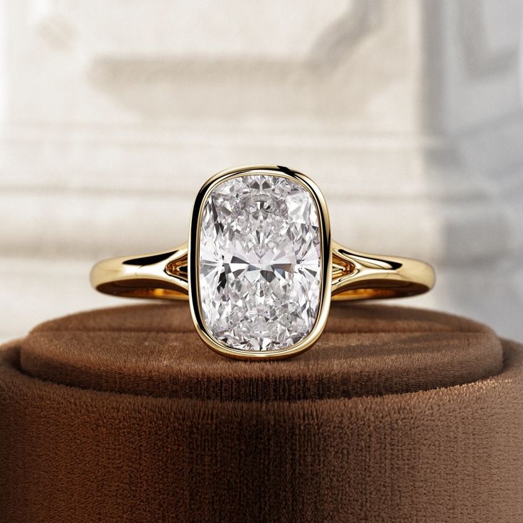 a cushion cut diamond ring sitting on top of a brown velvet covered display stand with a white marble wall in the background