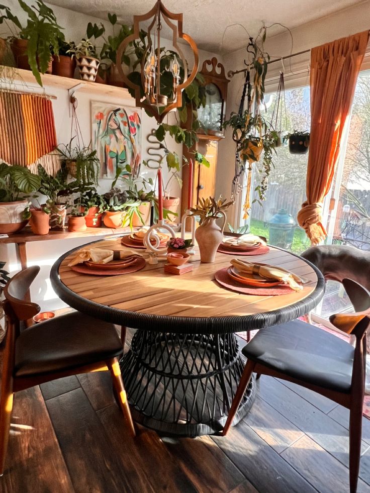 a dining room table set with place settings and potted plants