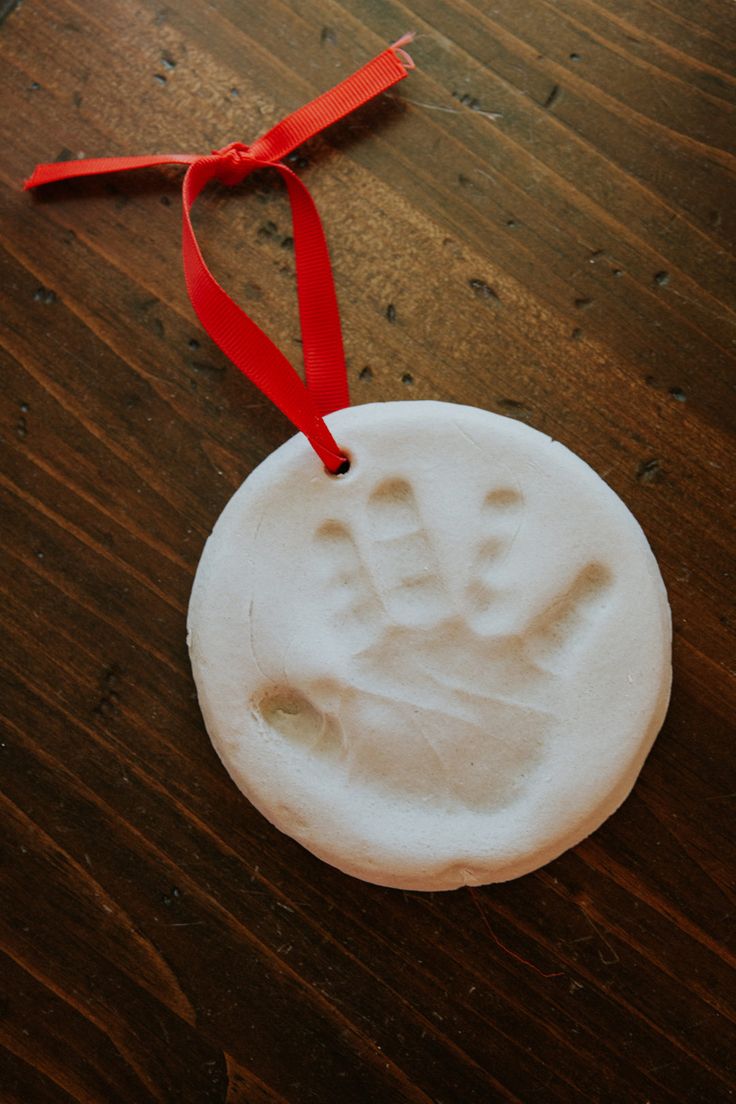 a handprint ornament on a wooden table with a red ribbon around it