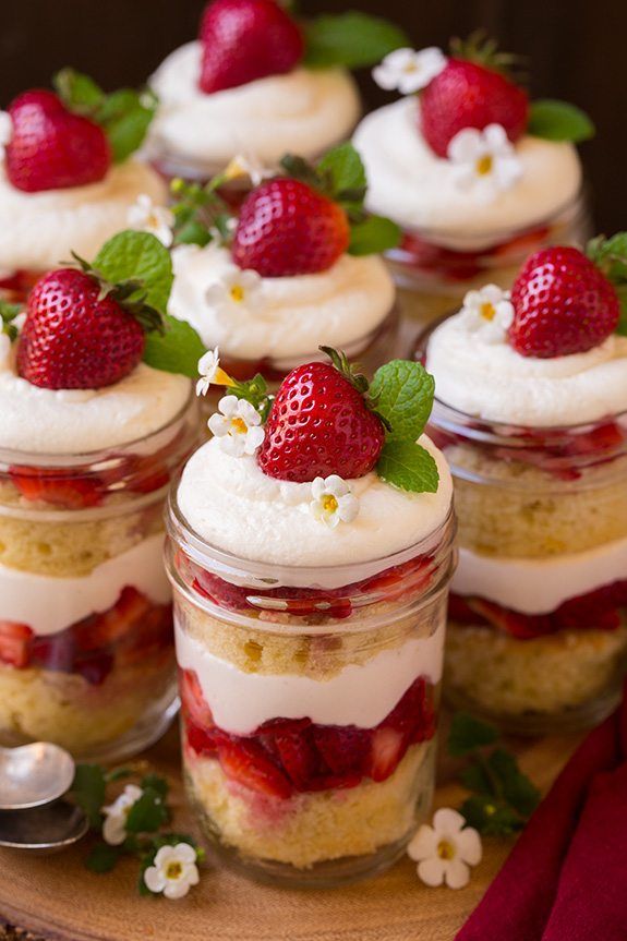 strawberry shortcakes with whipped cream and fresh strawberries in small glass jars on a table