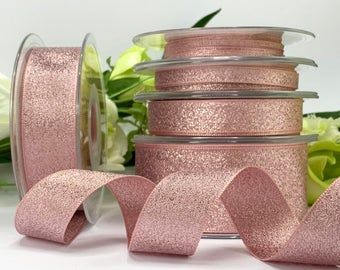 pink glitter ribbon on white background with flowers in the backgroung and three rolls