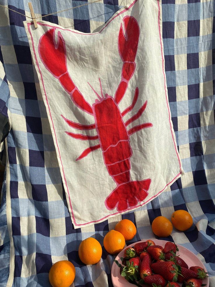 a red lobster on a blue and white checkered blanket with strawberries in front of it