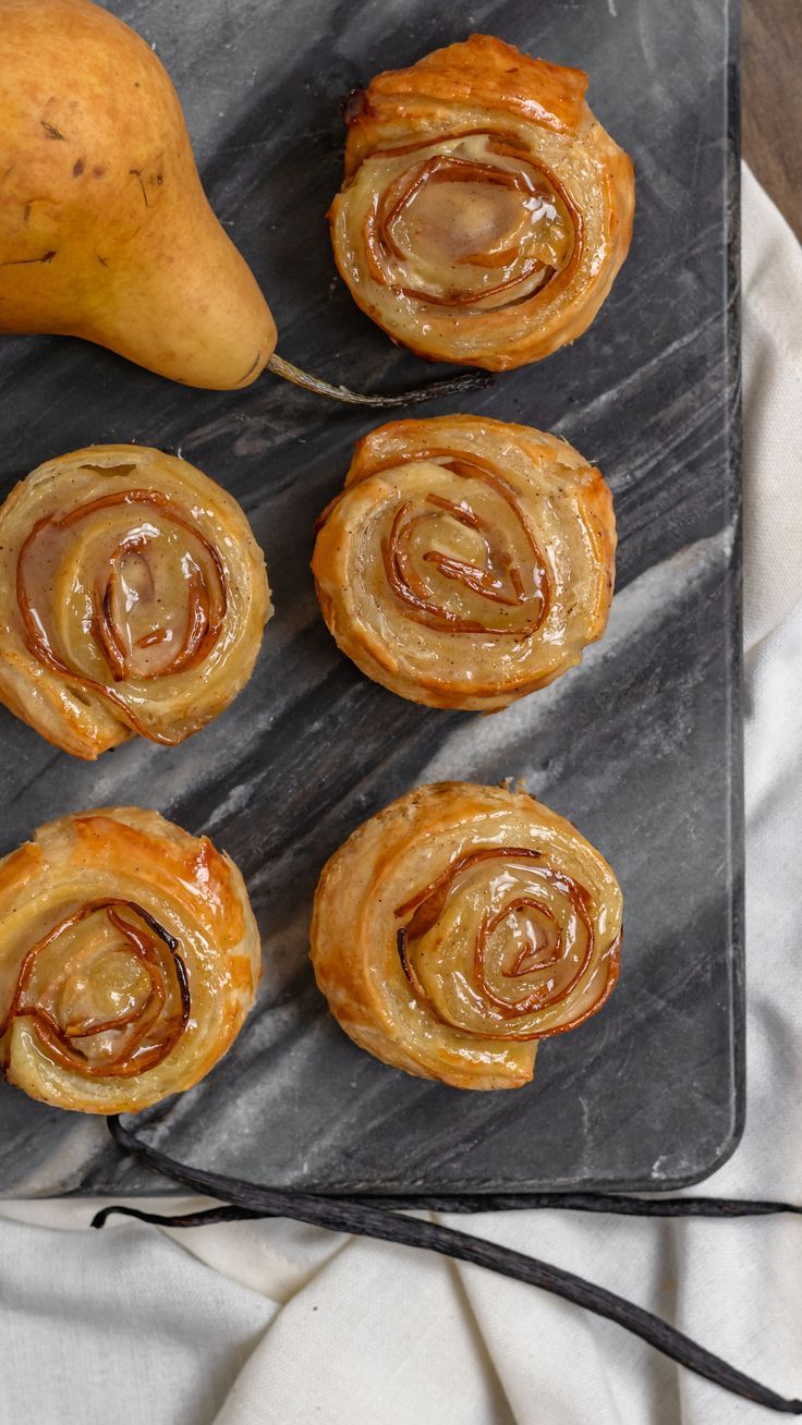 several pastries on a slate board with a pear and cinnamon roll in the background