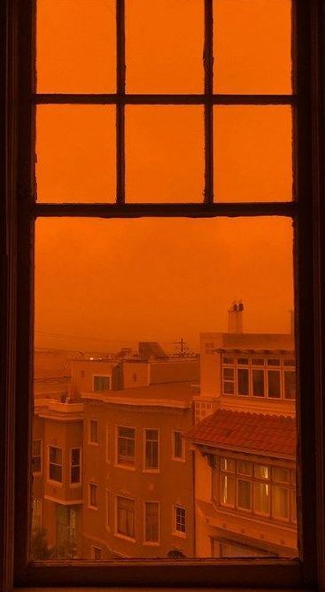 an orange sky seen through a window in a building with the view of buildings and rooftops