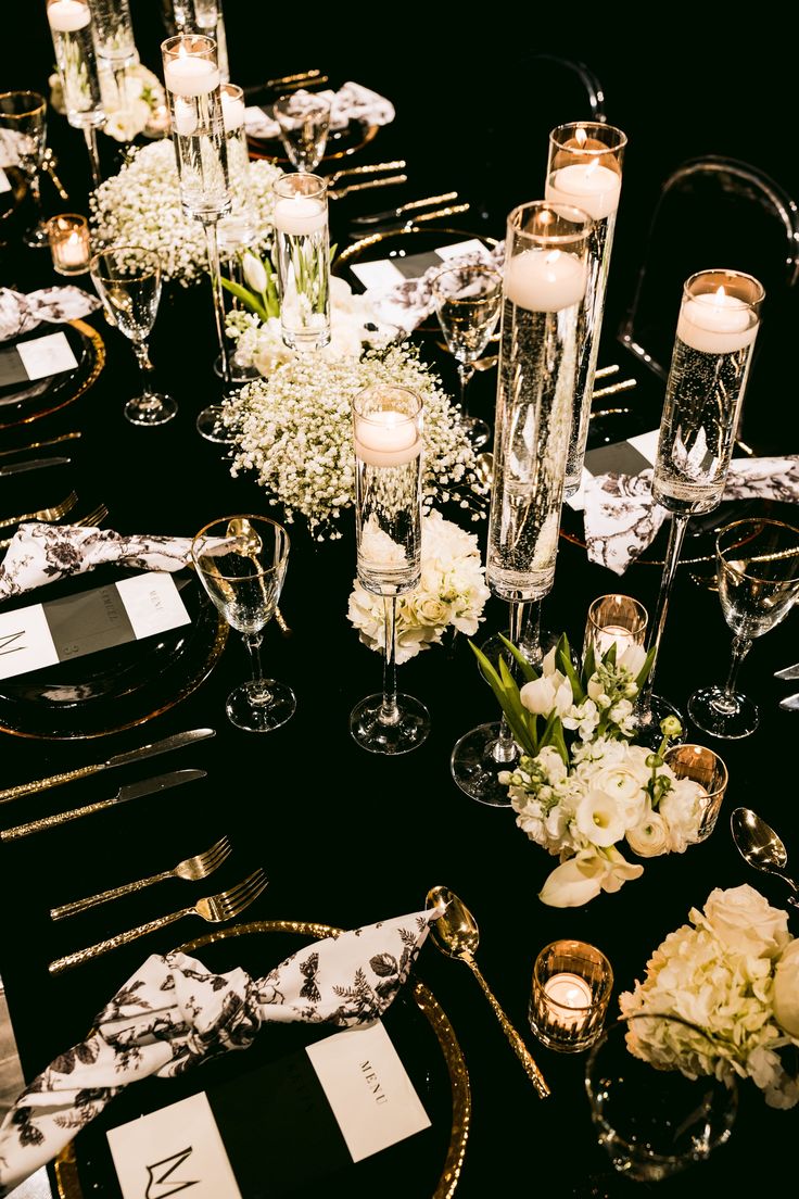 a black table topped with white flowers and candles