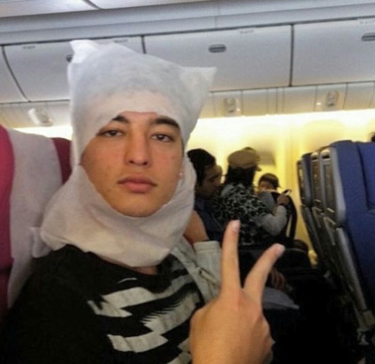 a woman with a bandage on her head sitting in an airplane pointing at the camera