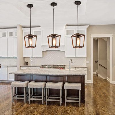 a kitchen with white cabinets and wooden flooring has four pendant lights hanging over the island