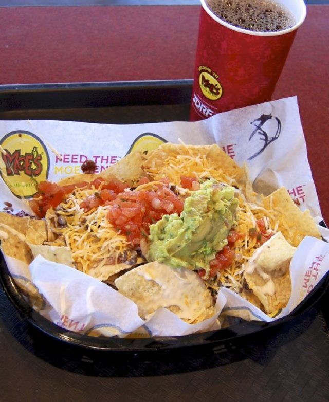 a tray filled with nachos and chips next to a cup of soda on a table