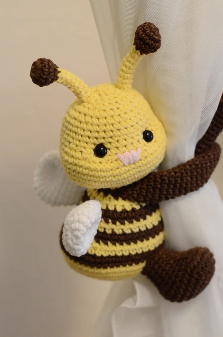 a crocheted yellow and brown stuffed animal hanging from the side of a curtain