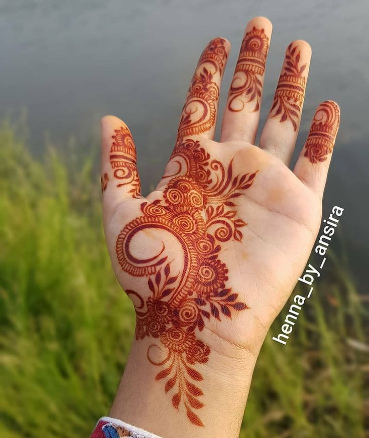 a person's hand with henna tattoos on it and grass in the background