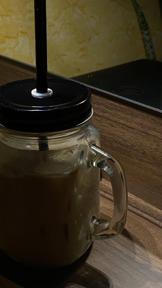 a glass jar with a black lid sitting on top of a wooden table next to a laptop