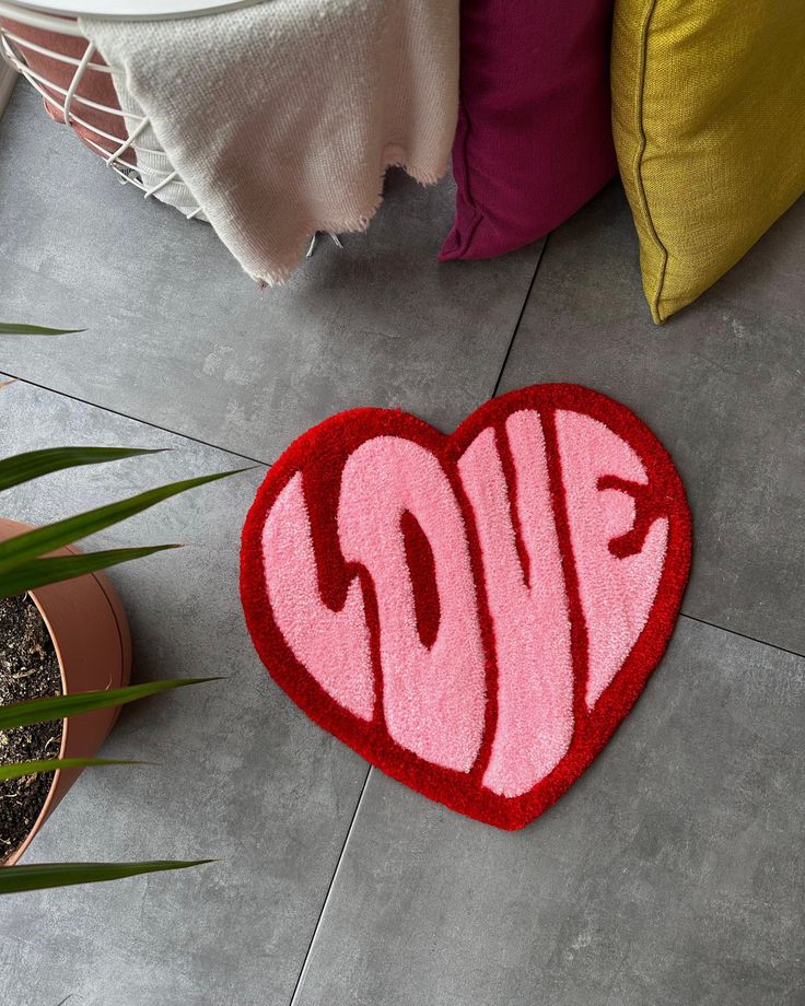 a heart shaped rug with the word love painted on it next to potted plants