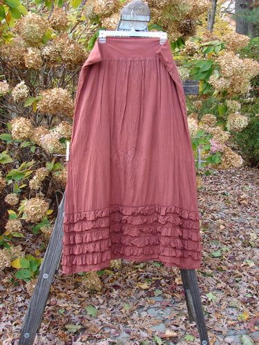 a red dress hanging on a clothes rack in front of some bushes and trees with leaves