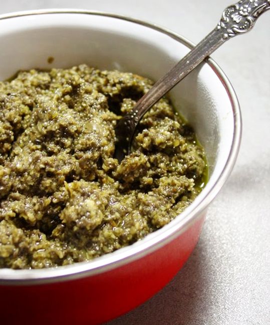 a red bowl filled with green food on top of a white table next to a silver spoon