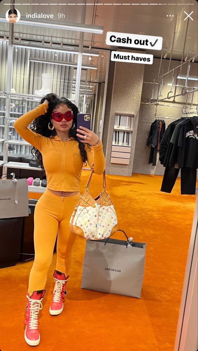 a woman taking a selfie with her cell phone in an orange outfit and sneakers