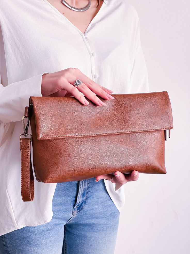 This foldover clutch is made of high quality vegan leather in brown. It has a zippered closure and it also has an invisible magnetic snap for extra security. It has a detachable wrist strap and  crossbody strap which is also detachable and adjustable. It has stain resistant lining and a zippered inside pocket. It also has an exterior back pocket.  Its vegan leather is very soft and lightweight but durable. This bag is suitable for daily use or formal events.  It comes in 3 different colors: Brow Brown Soft Leather Shoulder Clutch, Business Brown Shoulder Bag With Fold Over Clasp, Brown Handheld Pouch With Detachable Strap, Travel Clutch In Soft Brown Leather, Faux Leather Clutch With Removable Pouch, Brown Satchel Clutch With Detachable Strap, Brown Clutch With Detachable Strap, Brown Envelope Bag For Travel, Brown Soft Leather Satchel Clutch