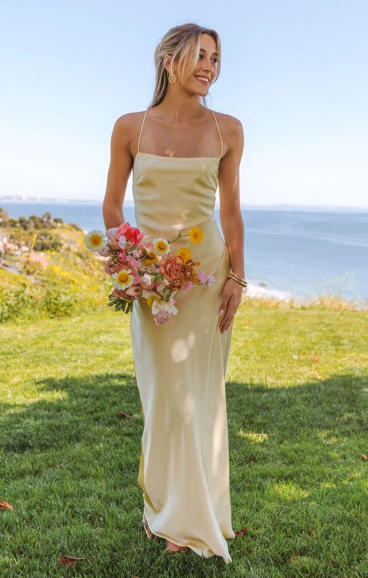 a woman standing in the grass holding a bouquet of flowers and smiling at the camera