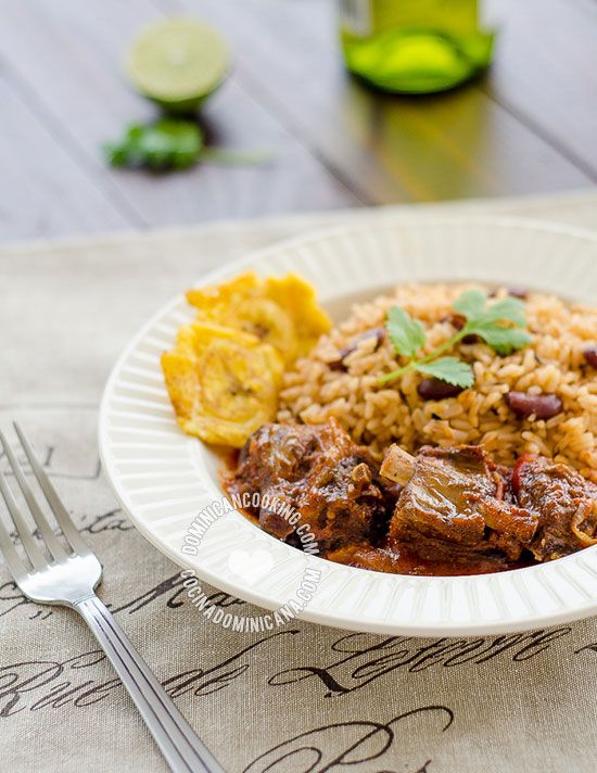 a white plate topped with meat and rice next to a fork, knife and napkin