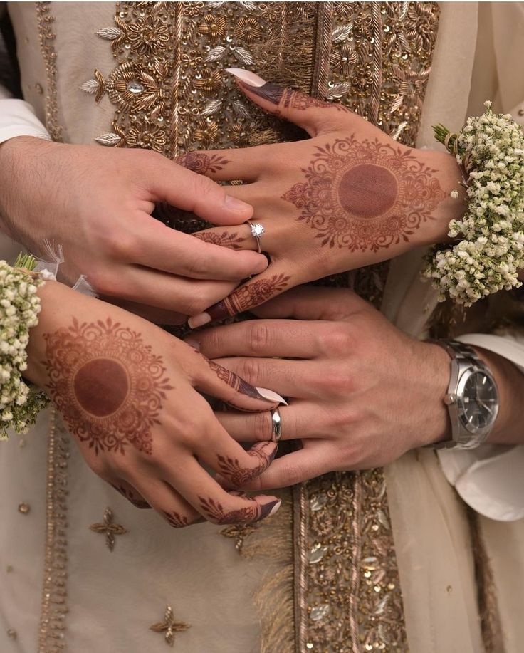 two brides with their hands covered in hendi and wedding rings, holding each other's hands