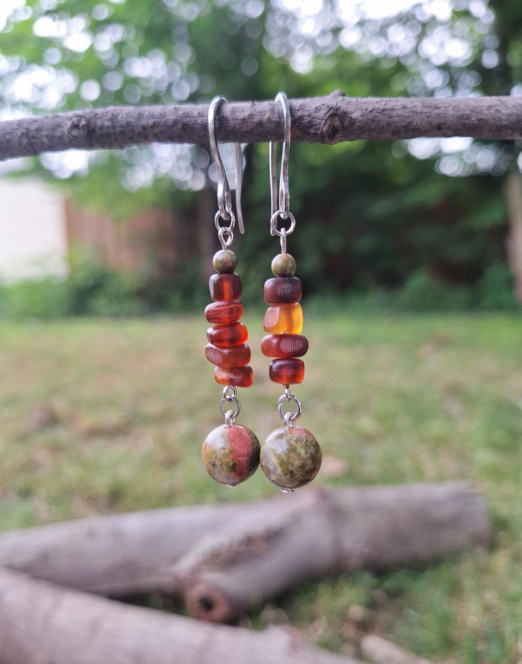 An earthy forest-inspired bohemian pair of silver dangle earrings; crafted with stainless steel French hooks, 4 mm polished unakite stone, brown sea glass, and a beautiful polished green unakite stone. *Handmade by me, one of a kind. *Length: 6 cm *Diameter of largest stone: 10 mm *Weight per Earring: 3 grams *Hook diameter: 1 mm *Crafted with silver stainless steel hypoallergenic hooks.  Nickel free. Click on the link below if you would like to see more artisan jewelry and unique artwork! https://www.etsy.com/shop/CailinCreatesCo I try my best to accurately portray the details in all of my jewelry. Please note that colors may vary due to lighting conditions, camera settings, and variations in computer monitor or phone display settings. If you have any questions regarding any items I have Adjustable Earthy Dangle Earrings, Handmade Adjustable Amber Earrings, Earthy Dangle Earrings With Ear Wire, Bohemian Amber Drop Earrings, Bohemian Amber Teardrop Jewelry, Bohemian Teardrop Amber Jewelry, Handmade Amber Bohemian Earrings, Handmade Bohemian Amber Earrings, Bohemian Amber Earrings With Ear Wire