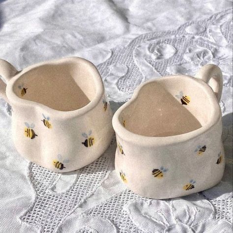 two ceramic cups with bees on them sitting on a white tablecloth covered bed sheet