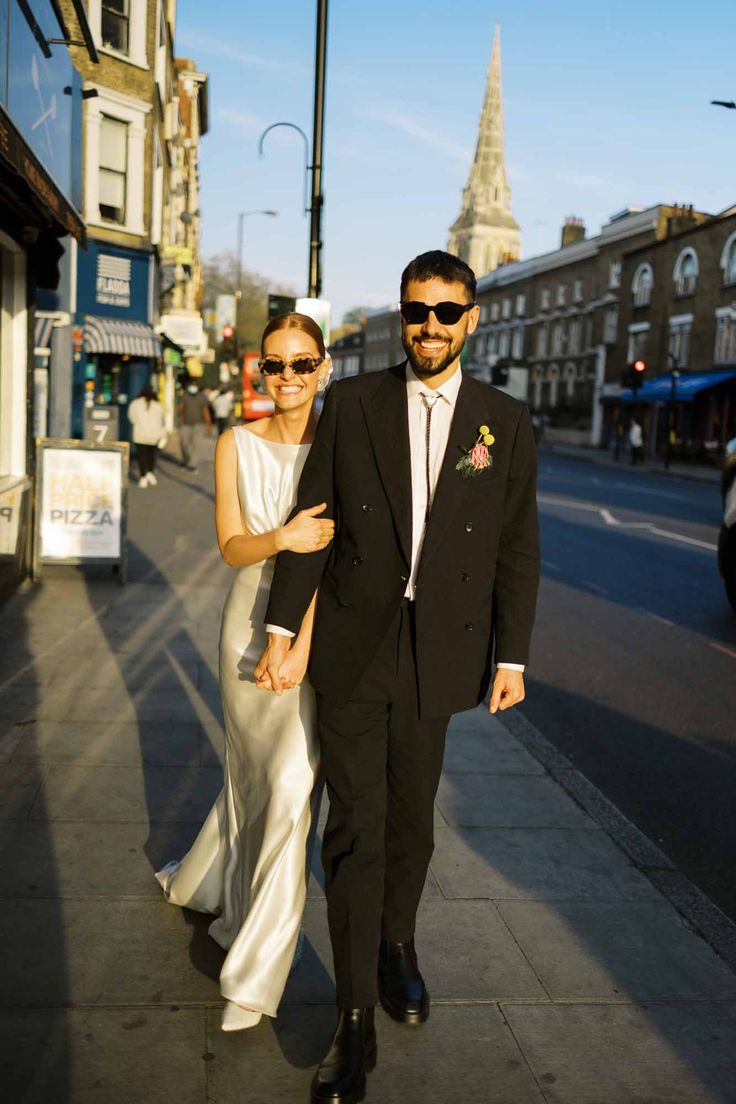 a man and woman are walking down the street in their wedding attire, one is wearing sunglasses