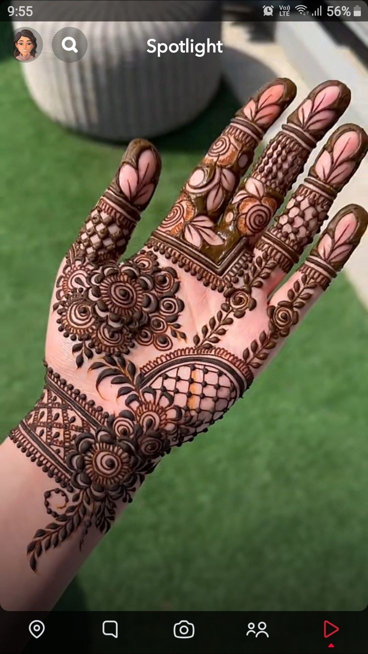 a hand with henna on it and some green grass in the backgroud