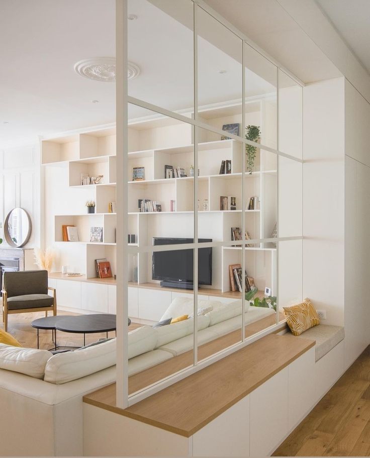 a living room filled with white furniture and lots of bookshelves next to a window