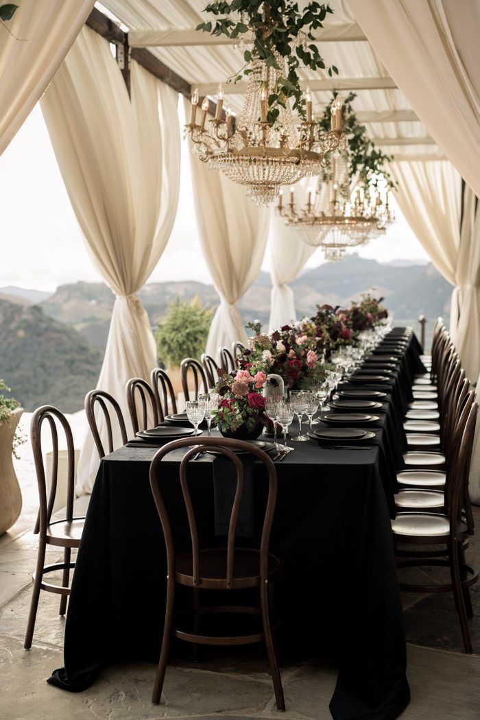 a long table with black cloths and white drapes is set up for a formal dinner